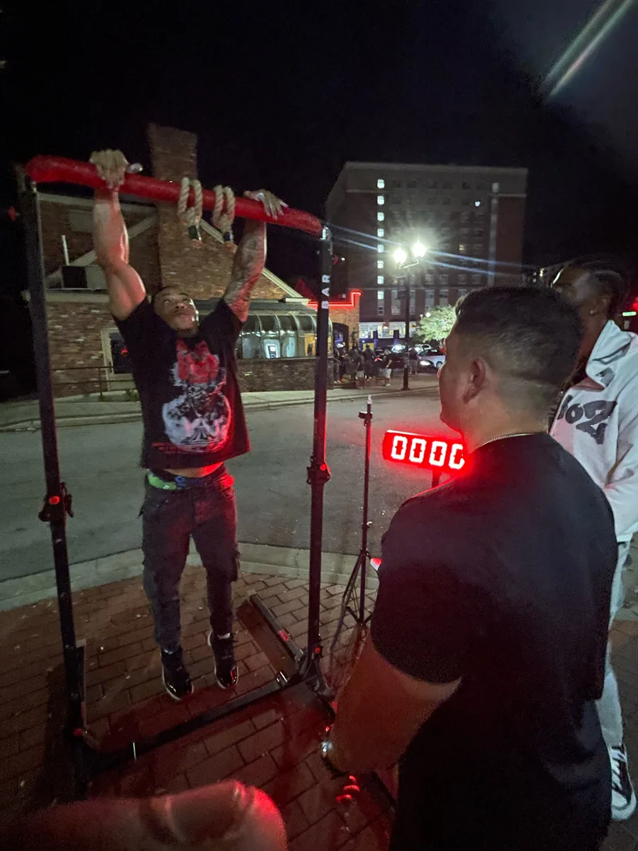 Challenger gripping the rope handles on the Arm Hang Challenge bar at night